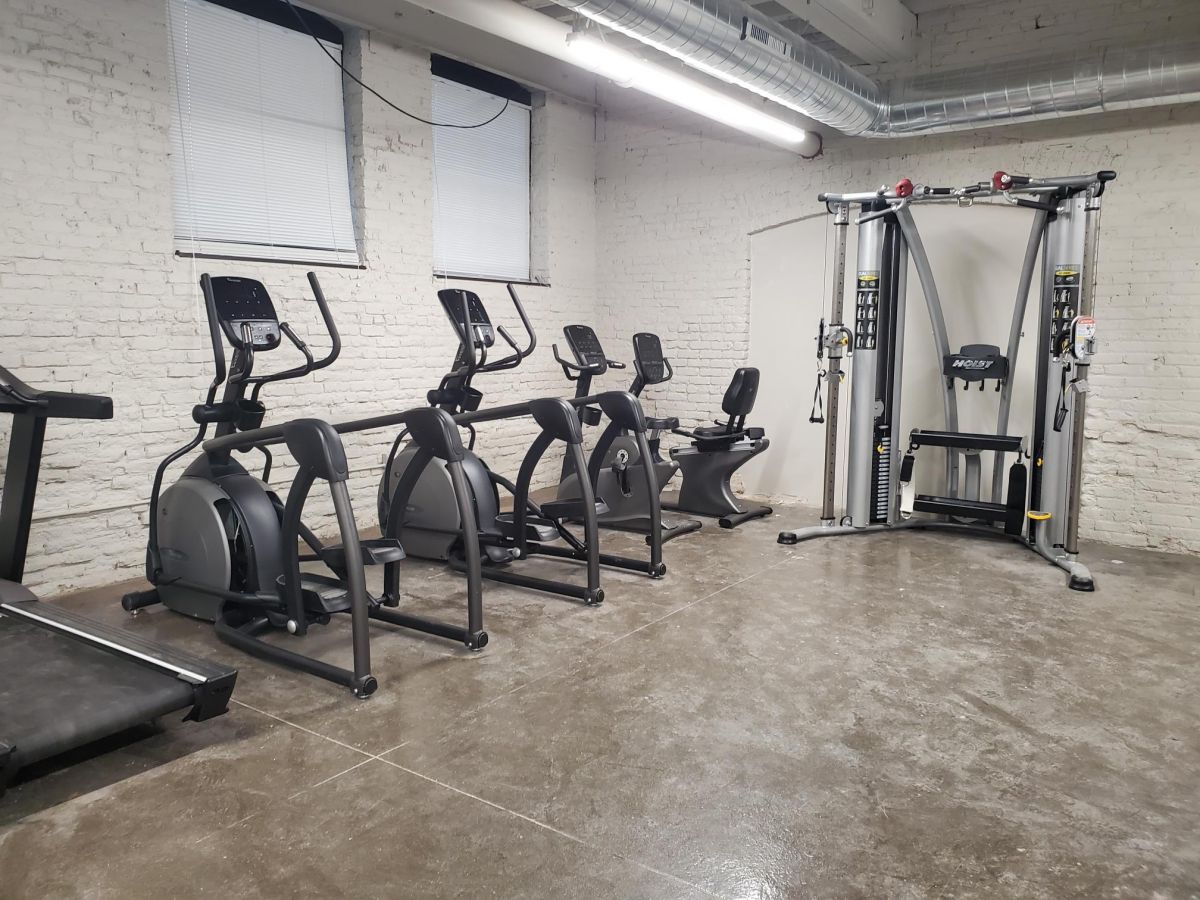 Three stationary bikes and a cable machine in a clean, minimalist gym with white brick walls.