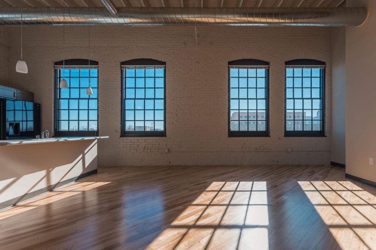 Sunny loft with four large windows, hardwood floors, and a modern kitchen area with pendant lights.
