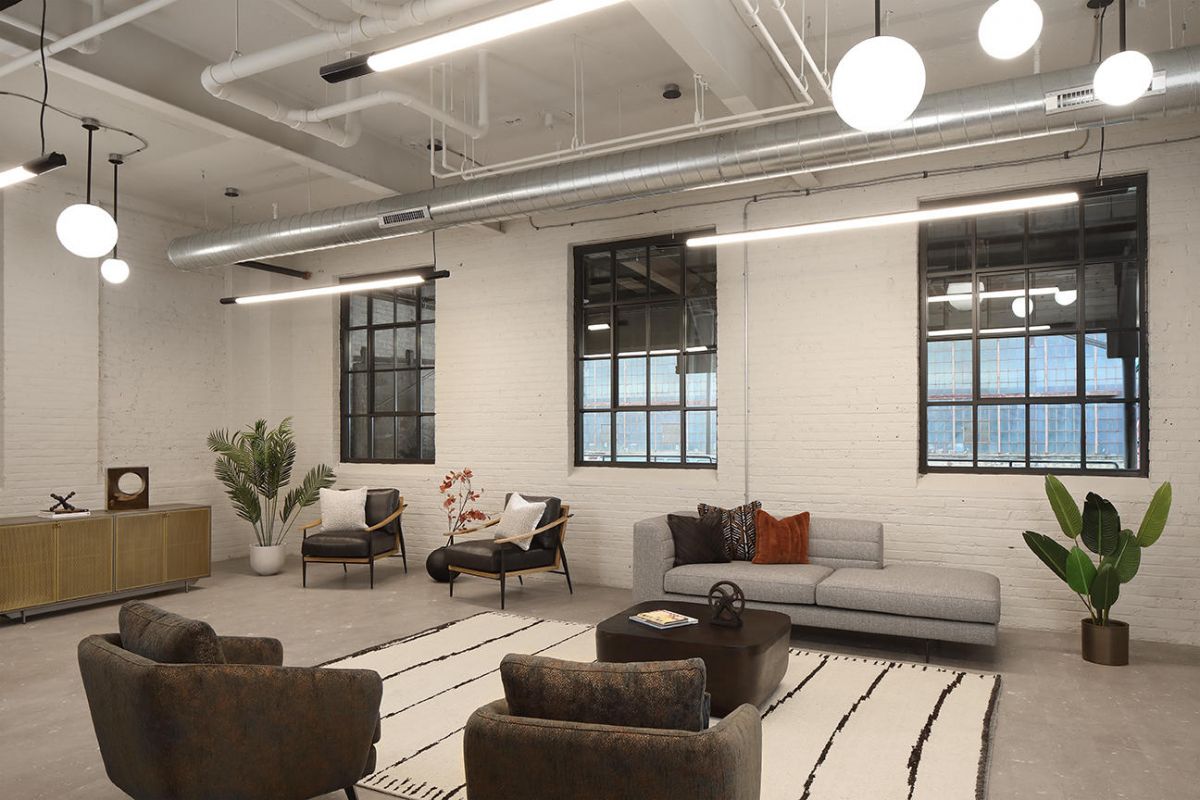 Modern lounge area with sofas, chairs, plants, and large windows in an industrial-style space.