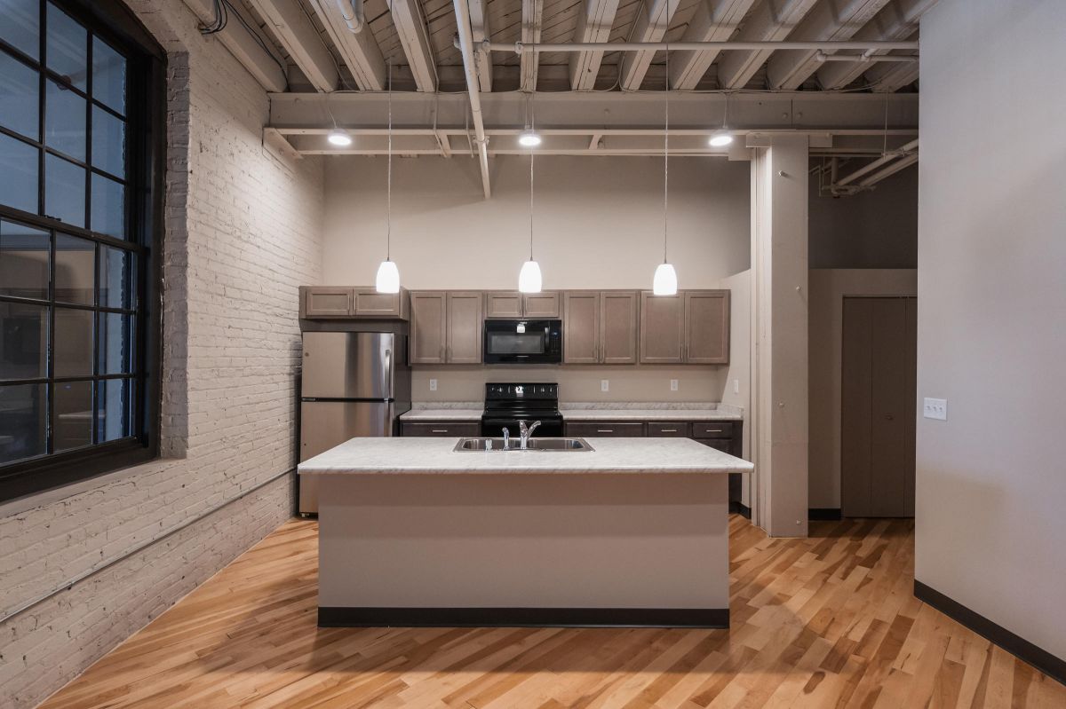 Modern kitchen with island, pendant lights, stainless steel appliances, and exposed ceiling beams.