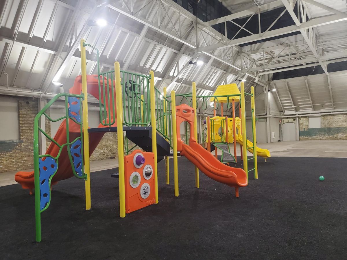 Indoor playground with slides, climbing features, and colorful equipment on a black floor under a high ceiling.